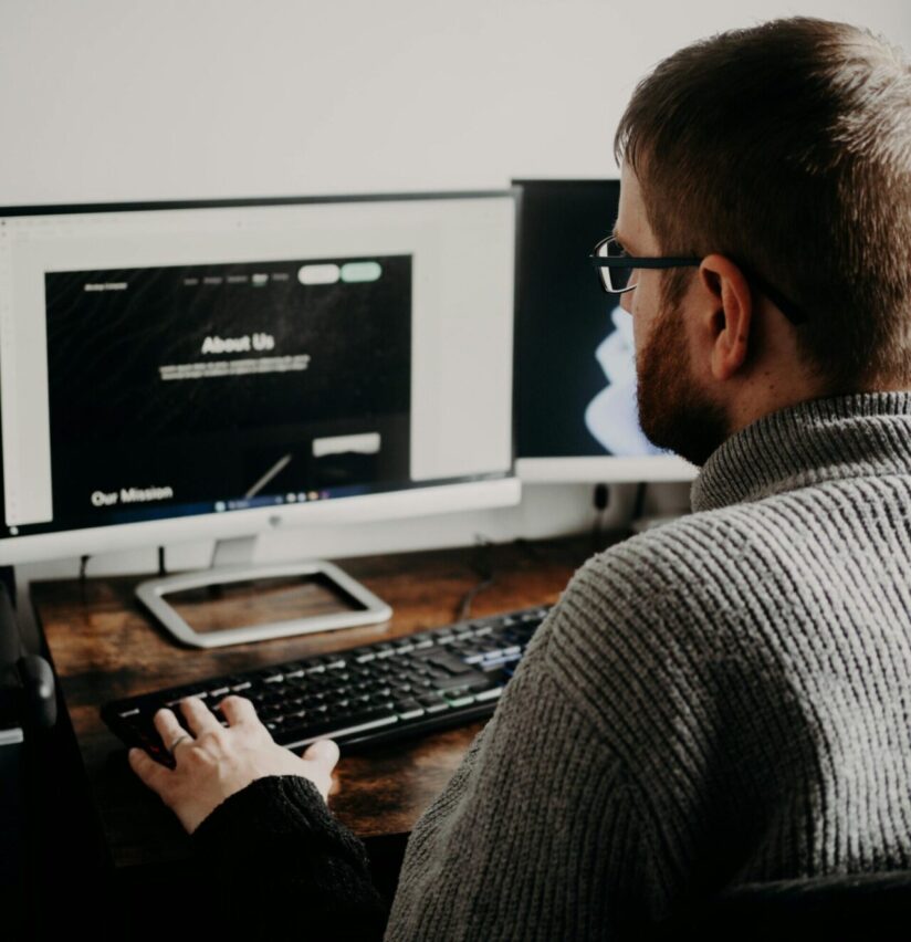 Man working on web design at home office setup with dual monitors.